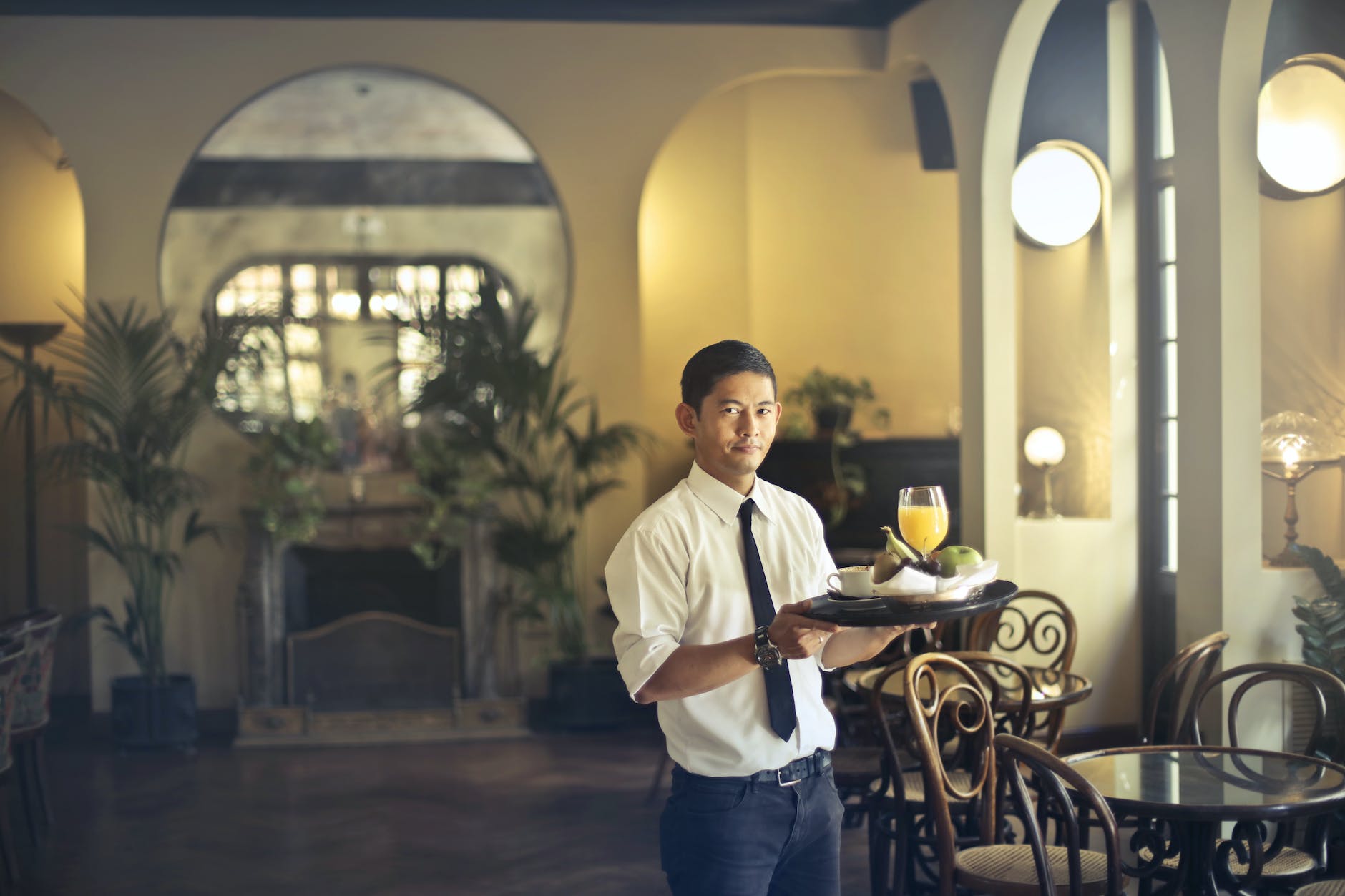 A waiter is delivering fruit and some drinks to a hotel table.